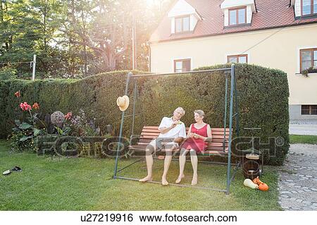 Stock Photograph - Senior couple, relaxing on swing seat in garden. Fotosearch