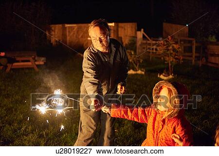 Stock Photo - Senior man in garden handing sparkler to girl. Fotosearch
