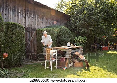 Stock Image - Senior man making wooden crate in garden. Fotosearch
