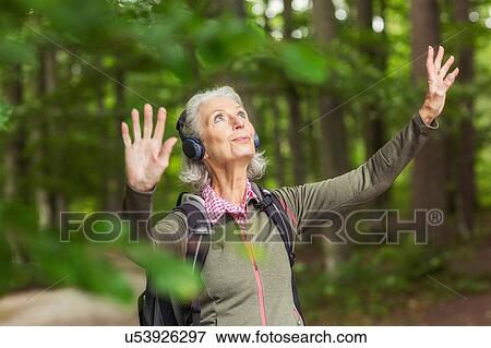 Senior woman in forest, wearing headphones, arms raised View Large Photo Image Stock Photo - Senior woman in forest, wearing headphones, arms raised. Fotosearch