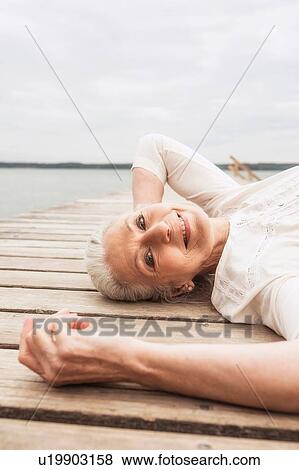 Senior woman relaxing on pier, smiling, elevated view View Large Photo Image Stock Photo - Senior woman relaxing on pier, smiling, elevated view. Fotosearch