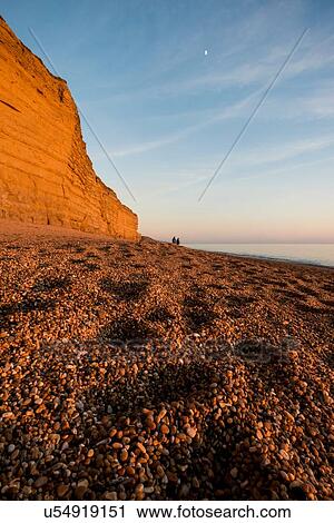 Stock Image - Shingle beach and cliffs at dusk, Burton Bradstock, Dorset, UK. Fotosearch