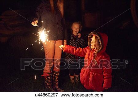 Side view of girl wearing red fur trim coat holding sparkler being ignighted by mother, smiling View Large Photo Image Stock Photo - Side view of girl wearing red fur trim coat holding sparkler being ignighted by mother, smiling. Fotosearch