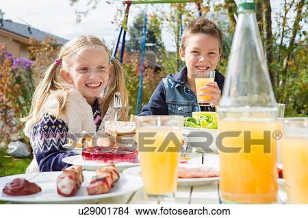 Picture - Sister and brother drinking juice at garden barbecue table. Fotosearch