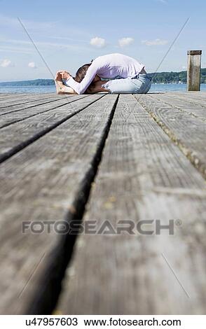 Surface level side view of mature woman sitting on pier bending over touching toes View Large Photo Image Stock Image - Surface level side view of mature woman sitting on pier bending over touching toes. Fotosearch