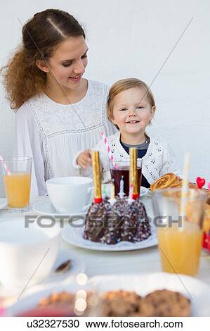 Stock Image - Teenage girl and toddler at patio table for birthday party. Fotosearch