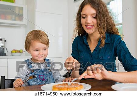 Teenage girl cutting cake for female toddler at kitchen table View Large Photo Image Stock Image - Teenage girl cutting cake for female toddler at kitchen table. Fotosearch
