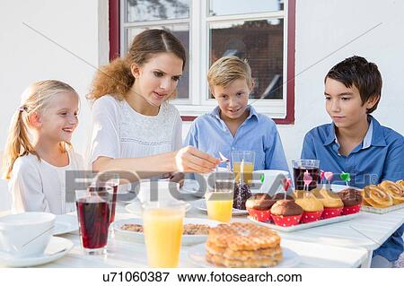 Stock Photo - Teenage girl lighting birthday cake candles for children at patio table. Fotosearch
