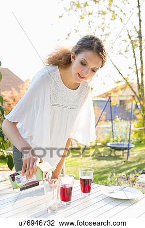 Stock Image - Teenage girl pouring fruit juice at patio table. Fotosearch