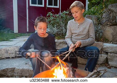 Two boys with sticks sitting by garden campfire at dusk View Large Photo Image Stock Photo - Two boys with sticks sitting by garden campfire at dusk. Fotosearch