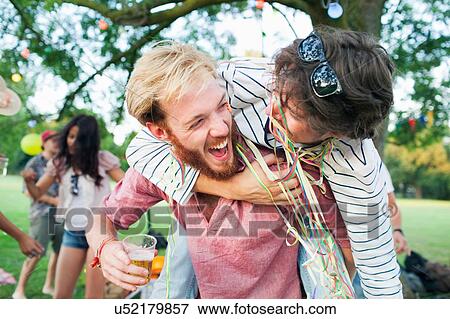 Stock Photo - Two male adult friends wrapped in streamers hugging at sunset party in park. Fotosearch