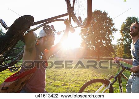 Stock Image - Two male friends arriving in park with bicycles at sunset. Fotosearch