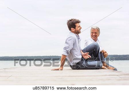 Two men sitting on pier, relaxing, smiling View Large Photo Image Stock Photography - Two men sitting on pier, relaxing, smiling. Fotosearch