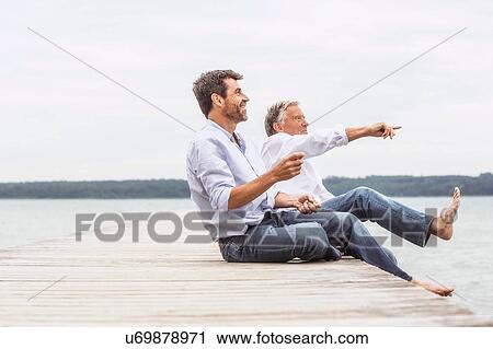 Two men sitting on pier, throwing stones, smiling View Large Photo Image Stock Image - Two men sitting on pier, throwing stones, smiling. Fotosearch