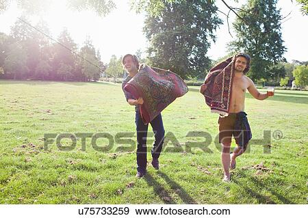 Stock Photo - Two young men carrying rugs for sunset park party. Fotosearch