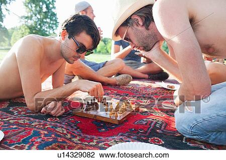 Stock Image - Two young men playing board game at sunset park party. Fotosearch