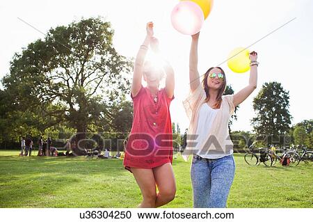 Stock Image - Two young women dancing with balloons at park party. Fotosearch