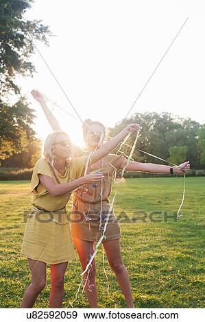 Two young women friends wrapping themselves in streamers at party in park View Large Photo Image Stock Photo - Two young women friends wrapping themselves in streamers at party in park. Fotosearch