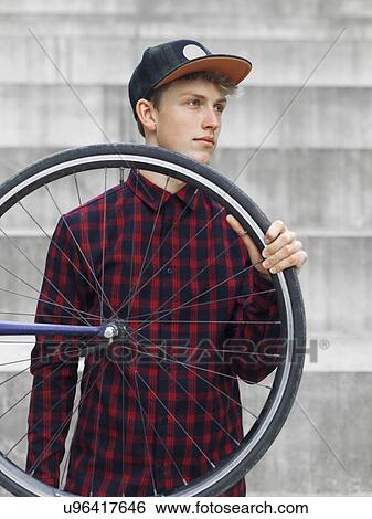 Stock Photograph - Urban cyclist carrying tyre in front of steps. Fotosearch