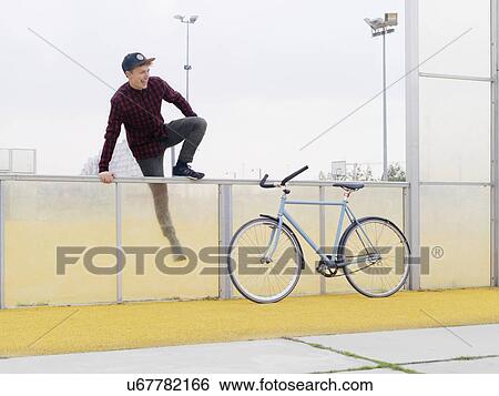 Urban cyclist climbing over fence on sports field View Large Photo Image Stock Photograph - Urban cyclist climbing over fence on sports field. Fotosearch