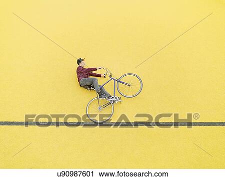 Urban cyclist doing illusionary stunt against yellow wall View Large Photo Image Stock Image - Urban cyclist doing illusionary stunt against yellow wall. Fotosearch