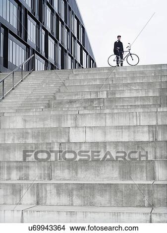 Urban cyclist with bicycle standing on top of stairway View Large Photo Image Picture - Urban cyclist with bicycle standing on top of stairway. Fotosearch
