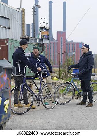 Stock Photo - Urban cyclists chatting near factory. Fotosearch