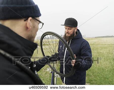 Stock Image - Urban cyclists fixing tyre in field. Fotosearch