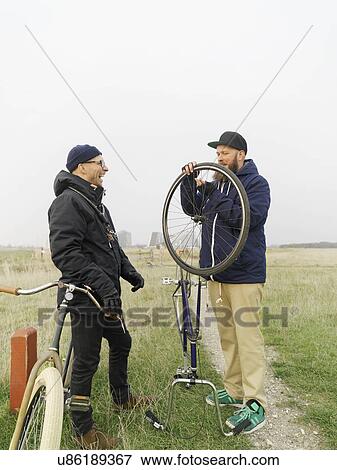 Stock Photo - Urban cyclists fixing tyre in field. Fotosearch