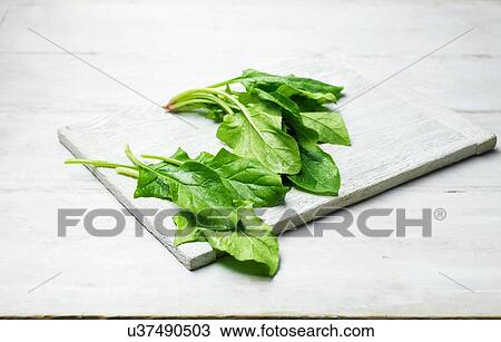 Stock Image - Whole leaf spinach on wooden chopping board. Fotosearch