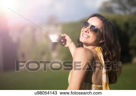 Stock Image - Woman looking over her shoulder posing with cup of tea at Thornbury Castle, South Gloucestershire, UK. Fotosearch