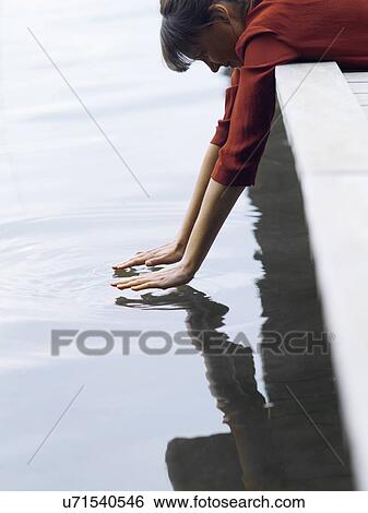 Stock Photograph - Woman lying on front hanging off pier touching surface of water, Copenhagen, Denmark. Fotosearch