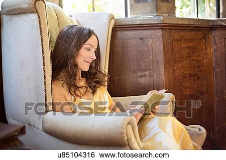 Stock Photograph - Woman reading book in old armchair at Thornbury Castle, South Gloucestershire, UK. Fotosearch