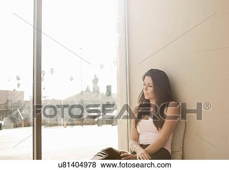Stock Photo - Woman sitting on chair beside window, looking out at snowy scene. Fotosearch