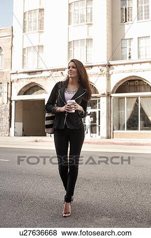 Woman walking in street, holding coffee View Large Photo Image Stock Photo - Woman walking in street, holding coffee. Fotosearch