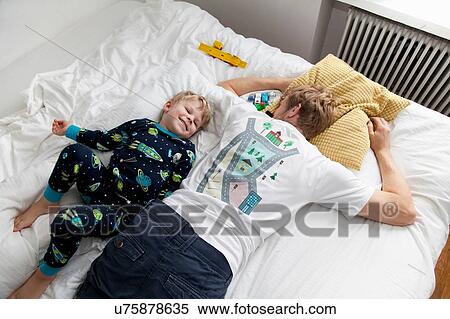 Young boy lying next to father n bed View Large Photo Image Stock Photography - Young boy lying next to father n bed. Fotosearch
