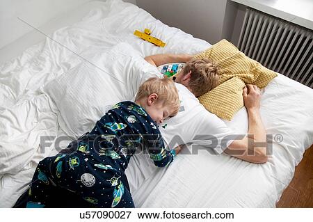 Stock Photo - Young boy lying on top of father n bed. Fotosearch