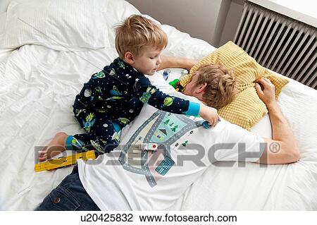 Stock Image - Young boy playing with toy car on back of fathers tshirt in bed. Fotosearch