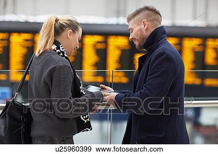 Stock Photo - Young couple at train station, looking at digital tablet. Fotosearch