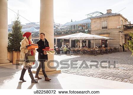 Stock Image - Young couple carrying xmas gifts strolling through Covent Garden, London, UK. Fotosearch