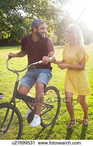 Young couple cycling in sunlit park View Large Photo Image Stock Image - Young couple cycling in sunlit park. Fotosearch
