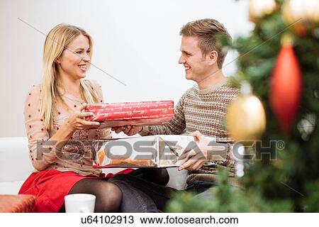 Stock Image - Young couple exchanging christmas presents in living room. Fotosearch