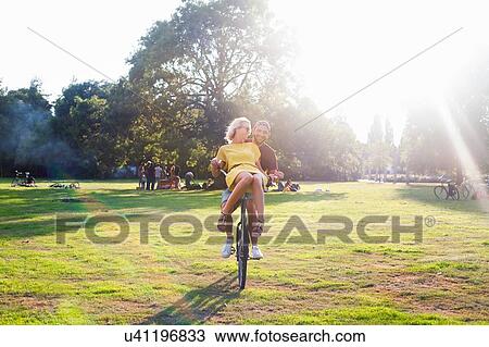 Young couple having fun on bicycle at sunset party in park View Large Photo Image Stock Image - Young couple having fun on bicycle at sunset party in park. Fotosearch