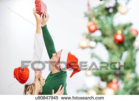 Young couple holding up and reaching for christmas present View Large Photo Image Stock Photography - Young couple holding up and reaching for christmas present. Fotosearch
