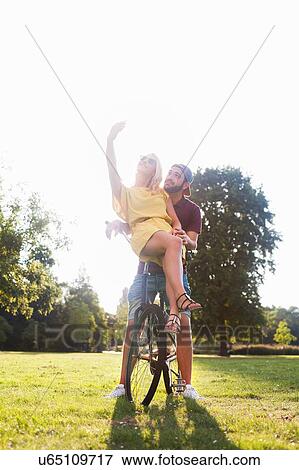 Stock Photo - Young couple on bicycle taking smartphone selfie in sunlit park. Fotosearch