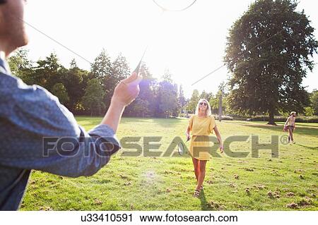 Stock Image - Young couple playing badminton in sunlit park. Fotosearch