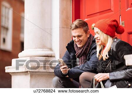 Young couple reading smartphone texts on doorstep, London, UK View Large Photo Image Picture - Young couple reading smartphone texts on doorstep, London, UK. Fotosearch