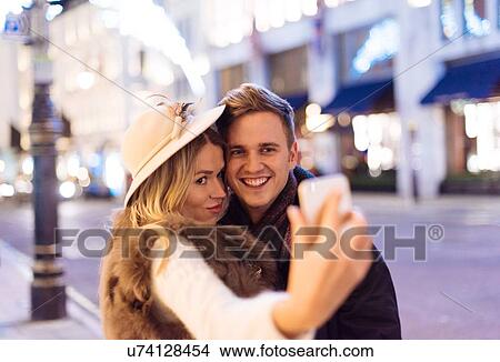 Young couple taking smartphone selfie at xmas on New Bond street, London, UK View Large Photo Image Picture - Young couple taking smartphone selfie at xmas on New Bond street, London, UK. Fotosearch