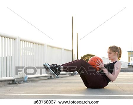 Stock Photo - Young female basketball player doing sit-ups in parking lot. Fotosearch