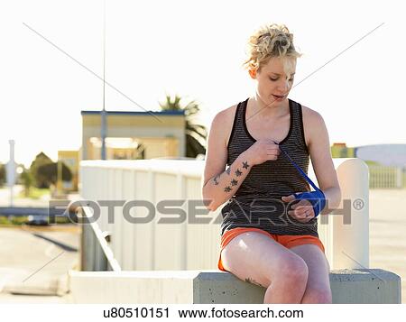 Stock Image - Young female boxer wrapping hands in bandage at parking lot. Fotosearch